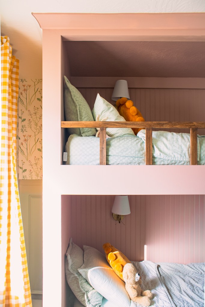 Cozy built-in twin over twin bunk beds with pink walls, featuring green bedding and stuffed animals, in a children's bedroom.