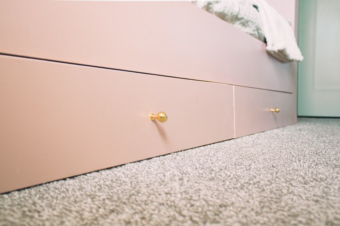 Close-up of the pink built-in bunk bed's storage drawers with gold knobs on a carpeted floor.