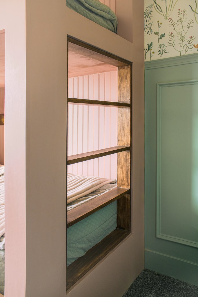 Interior view of a built-in twin over twin bunk bed with pink beadboard and a wooden ladder, featuring a cozy blanket on the top bunk.