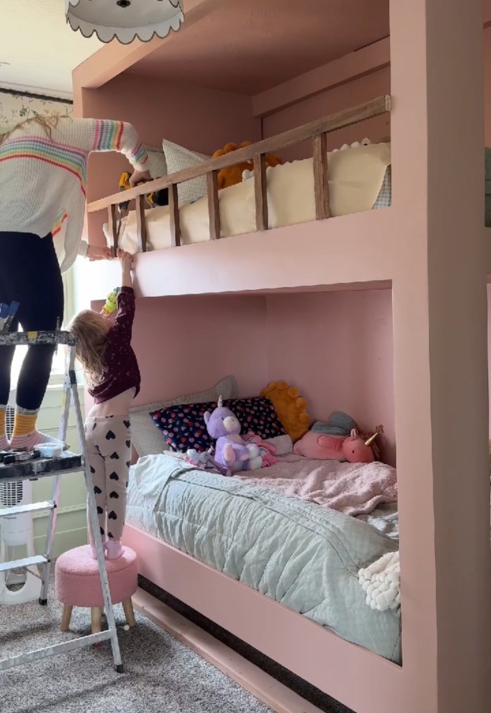 A child helping an adult adjust a safety railing on a built-in twin over twin bunk bed. The upper bunk is adorned with soft toys and bedding, while the lower bunk is decorated with plush animals and a cozy blanket. The room features a warm color palette and a playful atmosphere.