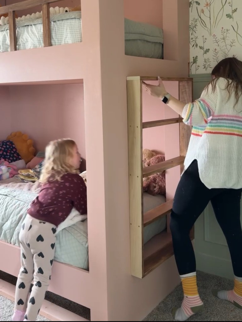 A child assists her mother with a custom-built twin over twin bunk bed featuring a pink paint finish and wooden accents, while the child playfully interacts with the lower bunk.